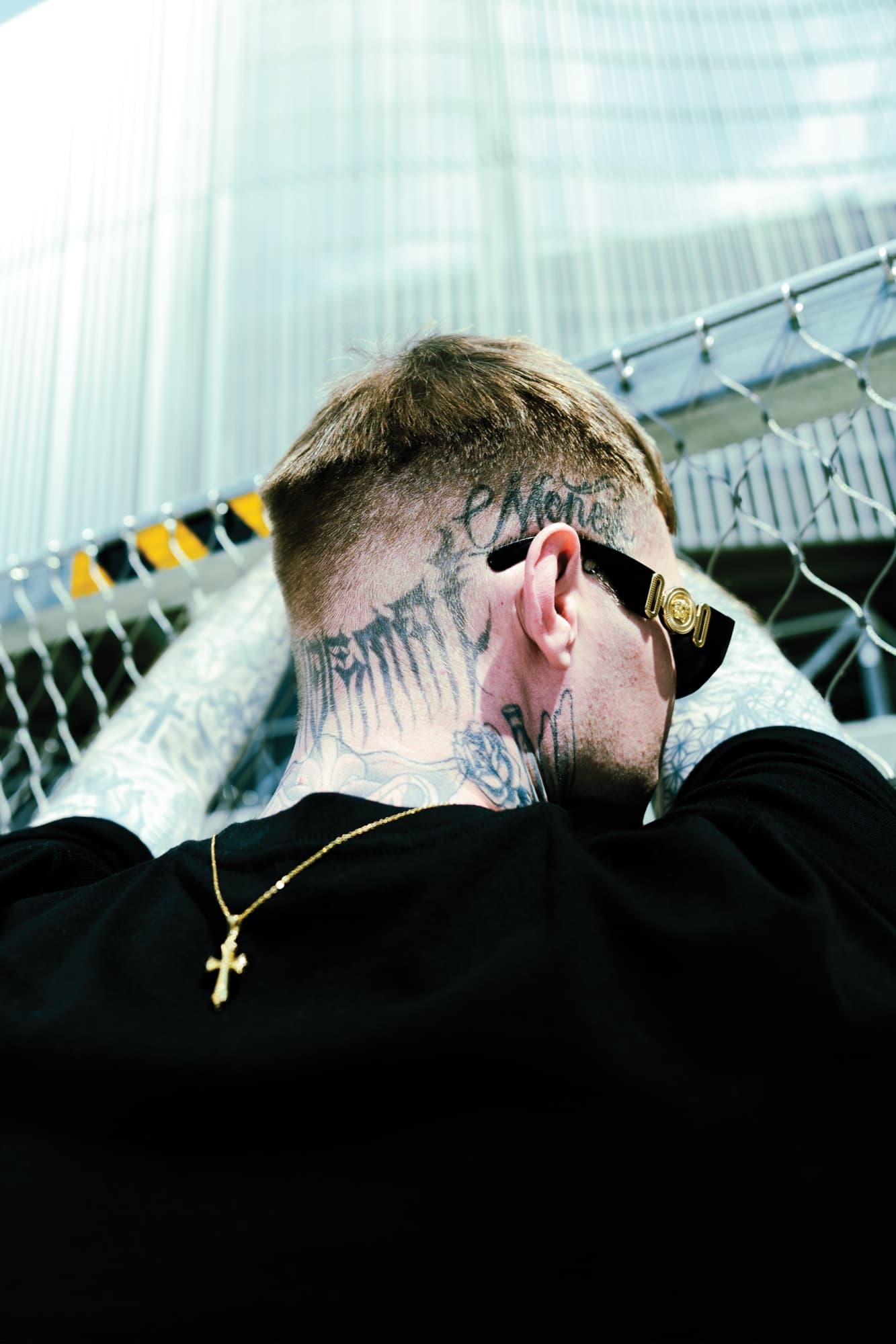 The back of the head – blackletter across the nape, gold cross catching the light.